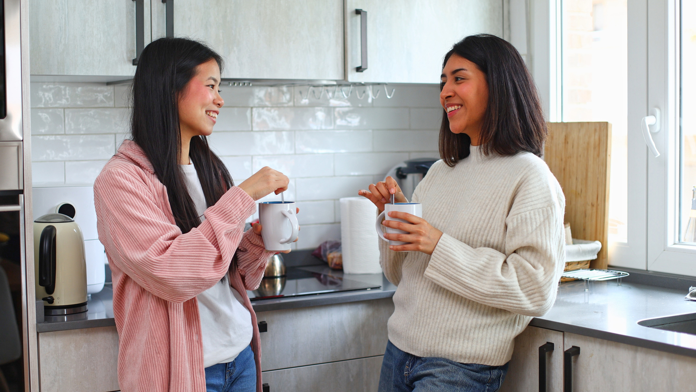 Two women talking over coffee in a bright kitchen.